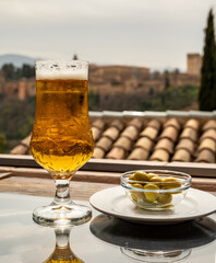 Spanish beer and glass bowl with green andalusian olives served on outdoor terrace with view on Sierra Nevada mountains in Granada, Andalusia, Spain
