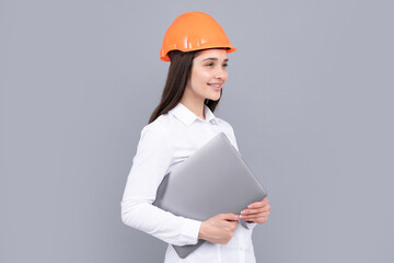 Young woman construction manager. Woman builder isolated portrait with protect helmet and laptop computer. Gray background, copy space.