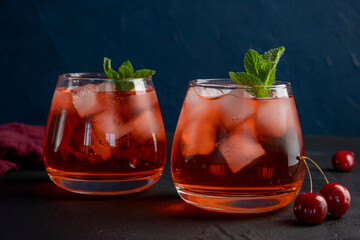 Cherry cocktail in glass on blue background. Summer iced beverage.