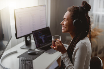 Side view of cheerful young female wearing headphones and programming on computer