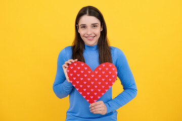 Love sign symbols for happy womens, valentines day or birthday. Happy woman hold red heart. Beautiful female model posing on isolated yellow background.