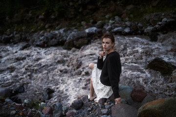 Lovely girl sits on the stone and poses next to the river. 