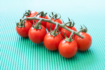 close up of a branch of cherry tomatoes on a green wavy background, vegan or vegetarian diet, fresh natural foods, complementary colors