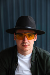 Happy fashion man. Portrait of handsome smiling stylish hipster lambersexual model. Man dressed in yellow sunglasses and black hat. Fashion male on the modern background. Caucasian. Guy