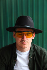 Man close eyes. Fashion man. Portrait of handsome smiling stylish hipster lambersexual model. Man dressed in yellow sunglasses and black hat. Fashion male on the modern background. Caucasian. Guy