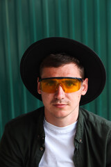 Happy fashion man. Portrait of handsome smiling stylish hipster lambersexual model. Man dressed in yellow sunglasses and black hat. Fashion male on the modern background. Stylish people. Boy. 20s