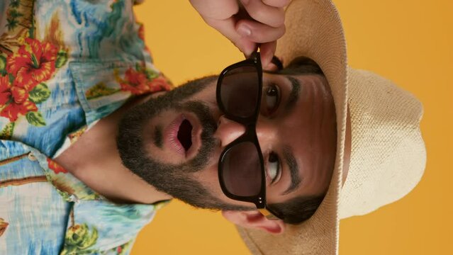Latin unshaved handsome young man dressed in a hat and a casual vacation shirt, removing his sunglasses and opening his mouth being shocked. High quality 4k footage