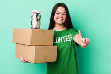 young adult woman smiling and looking friendly, showing number one. donation concept