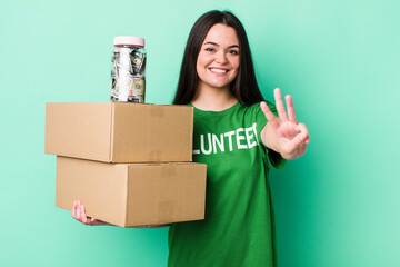 young adult woman smiling and looking friendly, showing number three. donation concept