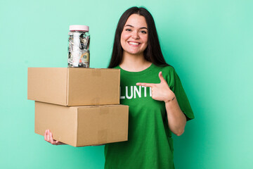young adult woman smiling cheerfully, feeling happy and pointing to the side. donation concept