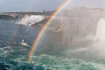 Rainbow over Niagara Falls with Maid of the Mist (small boat) on a sunny day.