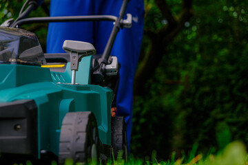 Lawn mowing. Technique and equipment for the garden.Green lawn mower close-up mows the lawn in the summer garden. Summer work in the garden. A man cuts green juicy grass with a lawn mower in a garden