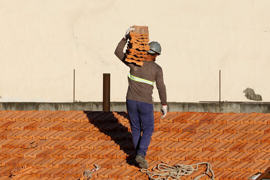 Roofer working on roofing construction. Bricklayer roof repair. House under construction. Workman renovates waterproofing roof of building. Carpenter construction worker carry pile of tiles