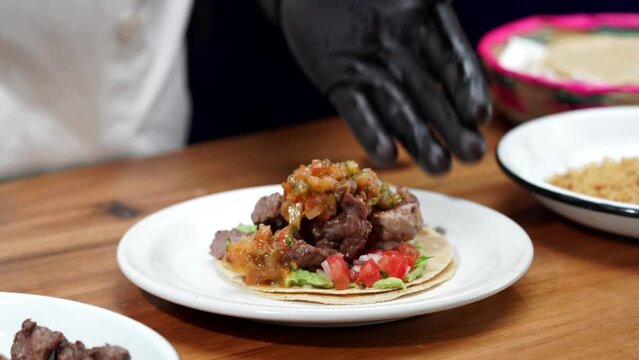 Mexican chef serving taco of beff on a blate from grill