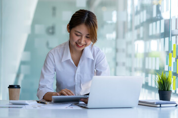 Happy Asian businesswoman laughing sitting at the work desk with laptop, a cheerful smiling female...