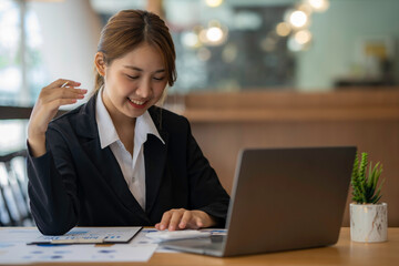 Happy Asian businesswoman laughing sitting at the work desk with laptop, a cheerful smiling female employee having fun feeling joy and positive emotion express sincere laughter at office workplace