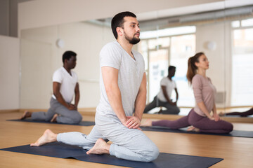 Caucasian man practising stretching asana with people during group yoga training.