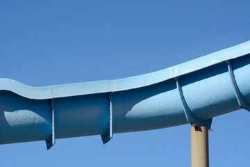 Blue water slide recreational equipment on pole against clear blue sky