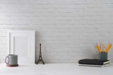 Contemporary workplace with picture frame, coffee cup, book and stationery on white table against brick wall. Copy space for your text.