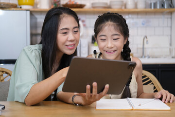 Asian mother helping her daughter doing homework with digital tablet at home..