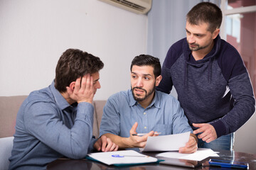 Three men having problems with some documents, worriedly discussing at home.