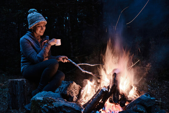 Woman enjoys a cold night in the forest sitting near a campfire