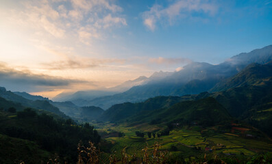 Obraz premium Dramatic sunset over mountain landscape. Beautiful landscape foggy hills twilight time. Blue golden sky sunrise dramatic beautiful landscape mountain. Dawn sky gold dusk time cloudscape with sunlight