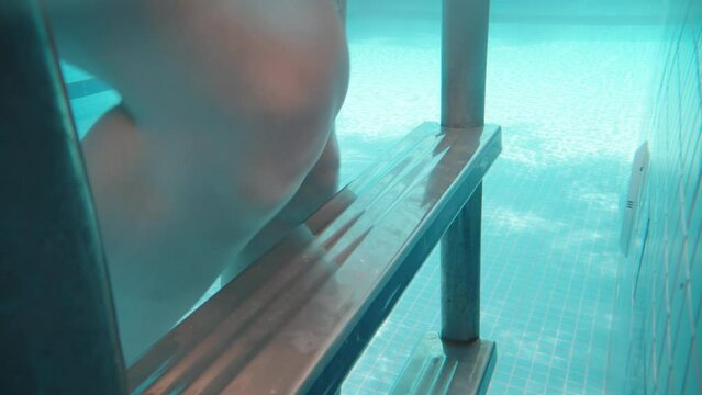 Blue swimming pool, underwater shooting, sunny day. A plump girl goes up the stairs from the water