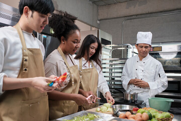 Hobby cuisine course, senior male chef in cook uniform teaches young cooking class students to peel...