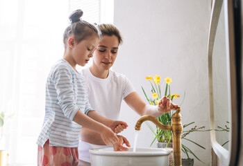 Young mother woman with long hair with little tween girl daughter in pajamas washing face and hands...