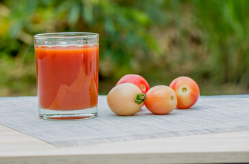 A glass of tomato juice is placed on the floor and the fruit of the tomatoes is beside it.
