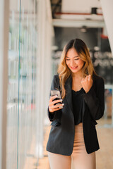 Asian businesswoman standing with smartphone and rejoicing at her success in office