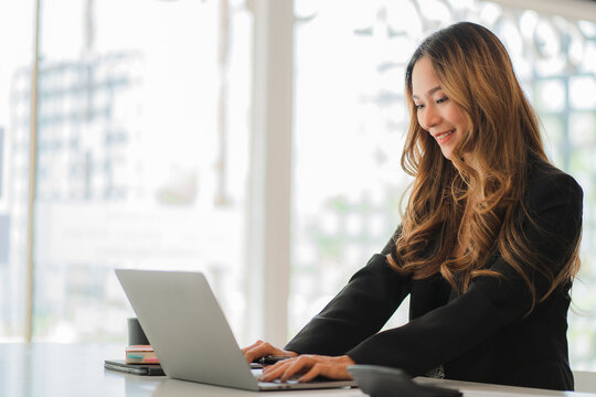 Smiling beautiful Asian businesswoman sitting with laptop and computer working on paperwork make an account analysis report real estate investment information financial and tax system concepts