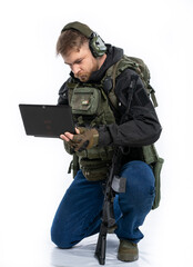 soldier, airsoft player in full gear works on a laptop in combat conditions. a man in headphones, a...