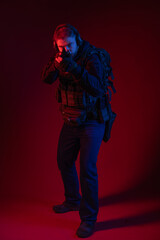 soldier in full gear with weapons. a man in headphones, body armor, with a backpack and a belt. red background. colored, blue-red light