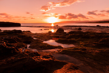 Gorgeous sunrise at seashore, sea puddles between rocks.