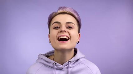 Modern young adult woman bringing closer to camera nodding head on violet color background. Stylish female individuality wearing trendy hoodie having funky look asking expressing agreement. Monochrome