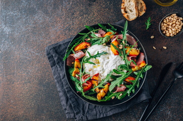 Heathy summer salad with grilled peach, arugula, ham and burrata.