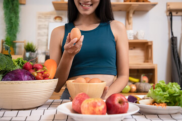 Young Asain beautiful woman holding fresh organic egg at home with surprise face in kitchen. Woman taking eggs and showing egg with happy face. Healthy homemade oatmeal