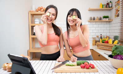 Sportsgirl beauty or good healthty concept. Young women cut cucumber for treatment and spa around eyes after doing yoga in kitchen. HealthcareMedical concept.