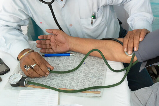 Howrah, West Bengal, India - 25th February 2018 : Indian male dotor checking blood pressure of a male patient and writing prescription.