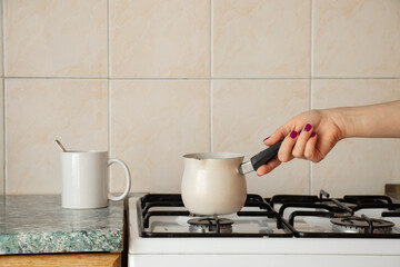 Turk on a gas stove and a white cup of coffee on a table in the kitchen at home, preparing morning coffee