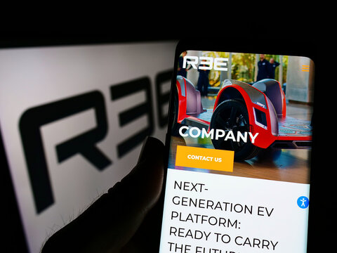 Stuttgart, Germany - 05-20-2022: Person holding cellphone with webpage of Israeli company REE Automotive Ltd. on screen in front of logo. Focus on center of phone display.