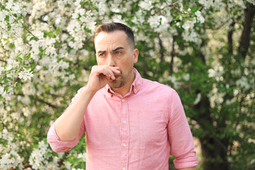 Portrait of a man feeling an itchy nose in the garden. Close-up of a man scratching his nose outdoors.