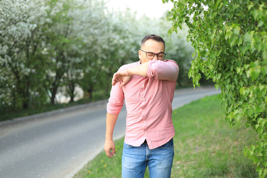 Young Sick Man Covering His Nose And Mouth With His Hand While Sneezing At Home. Sick Infected Female Patient Coughing In Her Elbow. Virus Protection. Proper Cough In Hands