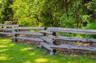 An old wood fence with a green field and forest. Wooden fence in a rural community park.