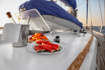 Fresh fruits with cold champagne and photo camera on deck of yacht - obrazy, fototapety, plakaty