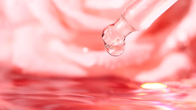 Pink serum fluid, oil drop from dropper falling in water on blurred rose flower