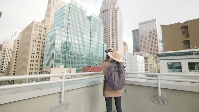 Back view of a woman taking photos of modern architecture. Female tourist shooting astonishing scenery of a typical American cityscape while standing on a rooftop. High quality 4k footage