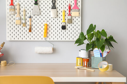 Desk with paint samples, houseplant and pegboard with tools on light wall